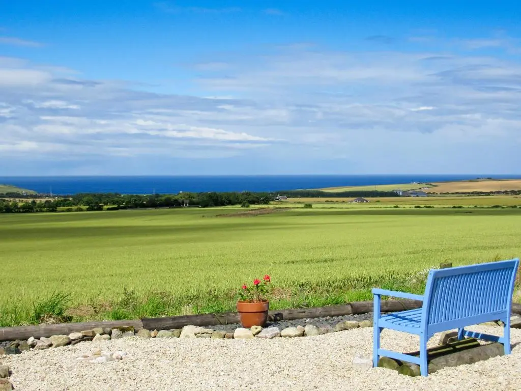 a blue bench sitting in front of a green field at The Brae Steading in Fordyce