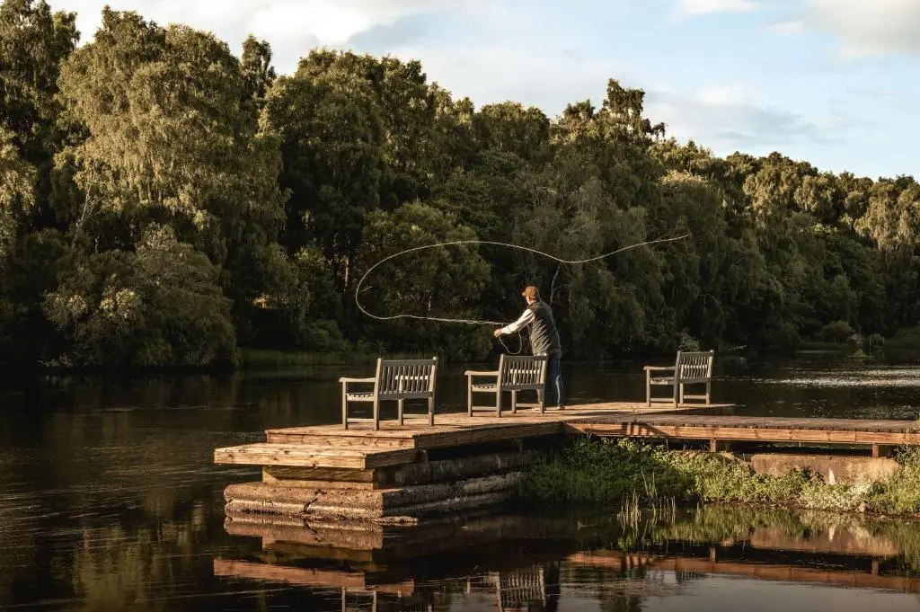 a man standing on a dock holding a fishing rod at Swiss Chalet Balnagown Castle in Kildary