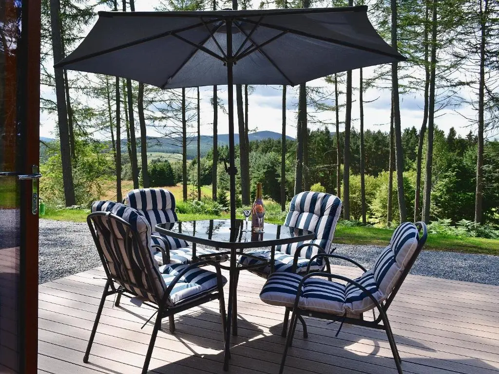 a table with four chairs and an umbrella on a deck at Mountshade in Finzean