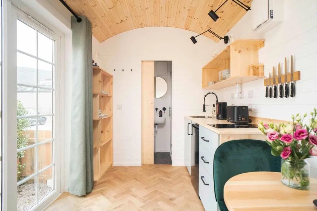 a kitchen with white counters and a table with flowers at Willow's Nordic Shepherds Hut in Ballater