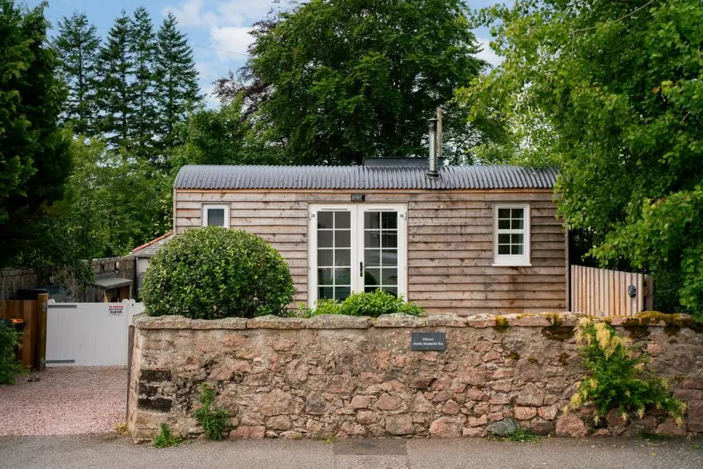 a small house behind a stone wall with a fence at Willow's Nordic Shepherds Hut in Ballater
