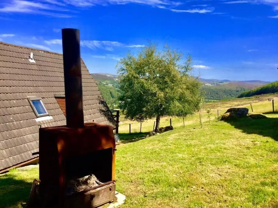 a view of a house with a field and a tree at Glen Lodges Rogart in Rogart