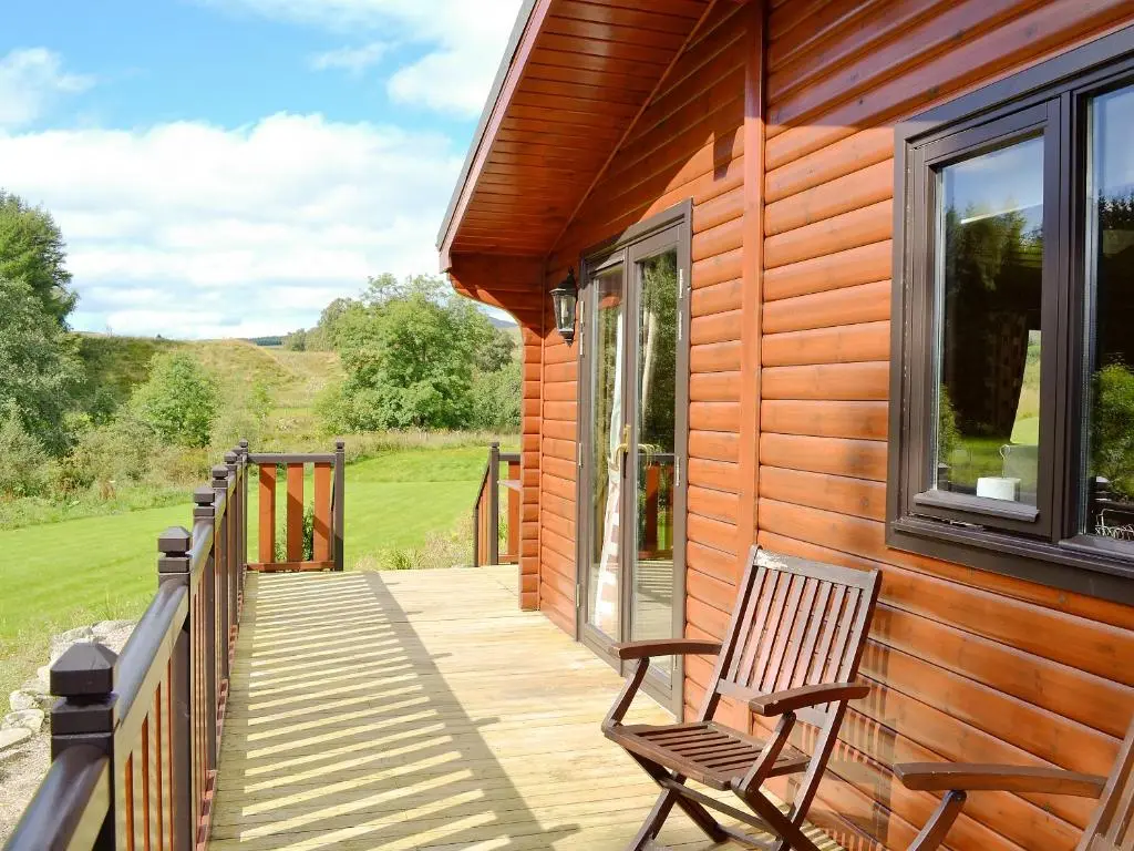 a wooden deck with a chair on the side of a house at Larch Cottage - S4428 in Kirkton of Glenisla