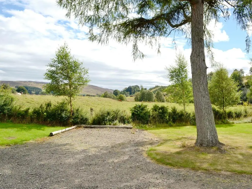 a gravel parking lot next to a tree at Larch Cottage - S4428 in Kirkton of Glenisla