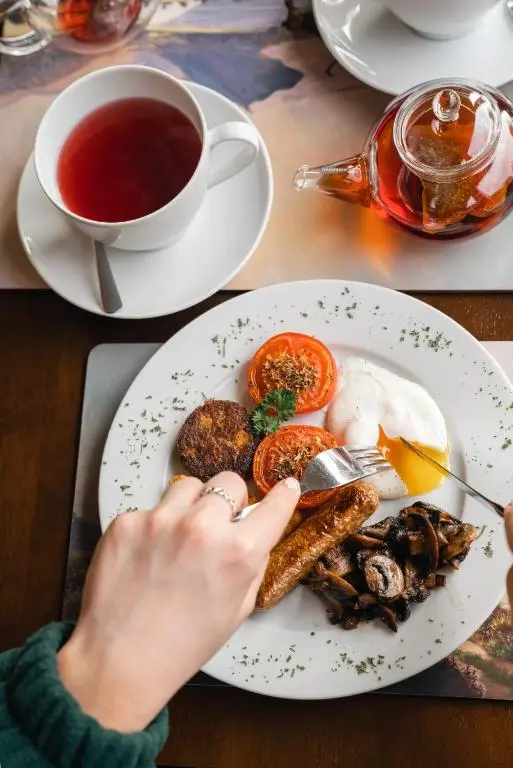 a person eating a plate of food with a cup of tea at Eriskay Guest House and Aviemore Glamping in Aviemore