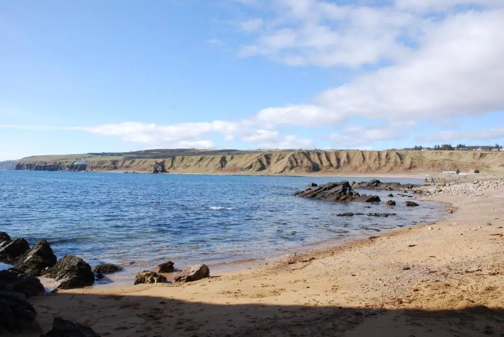 a beach with rocks in the water and a mountain at Turadh 'a break in the clouds' in Dunbeath
