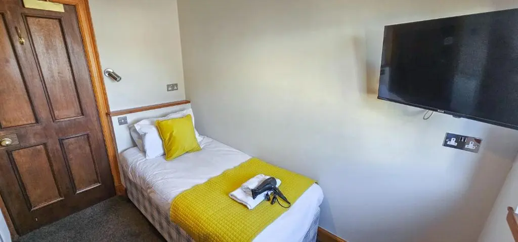 a room with a small bed with a yellow pillow and a television at Melrose Villa 11 Bedroom House in Inverness