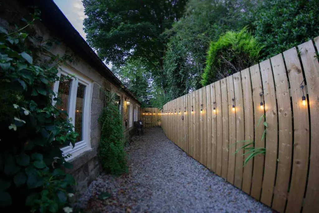 a fence next to a house with lights on it at The Potted Pineapple in Oyne