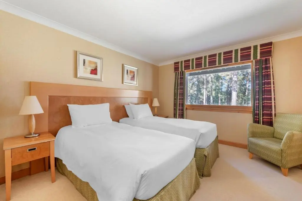 a bedroom with two beds and a chair and a window at The Lodges at Craigendarroch Country Club in Ballater