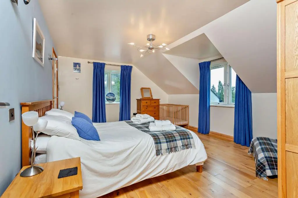 a bedroom with a large bed with blue curtains at Sealladh an Loch in Foyers