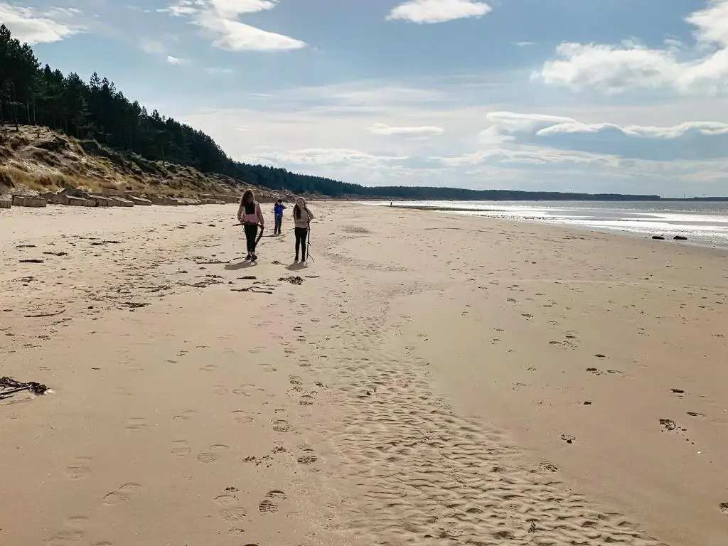 three people walking on a beach with footprints in the sand at Emerald Cottage in Burghead