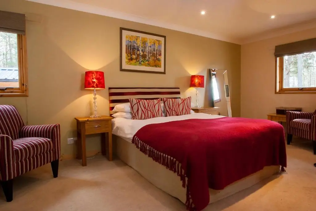 a bedroom with a bed and two chairs and two lamps at Riverside Lodge Garden Apartment in Aviemore