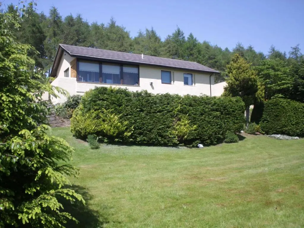 a house with a hedge in front of a yard at Achnacarry Cottage in Evelix