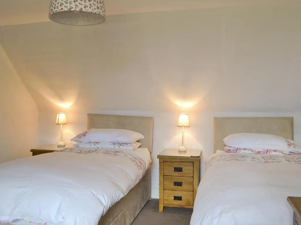 two beds in a room with two lamps on tables at Old Post Office House in Knockbain