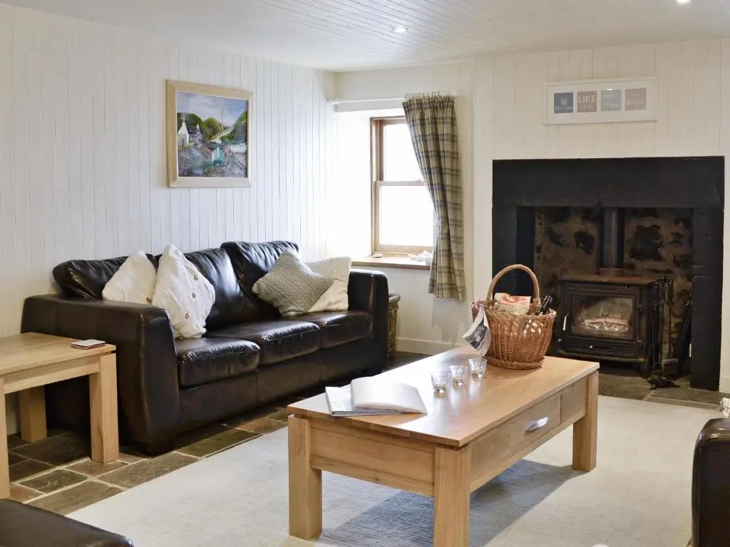 a living room with a black leather couch and a coffee table at Crovie Cottage in Gardenstown