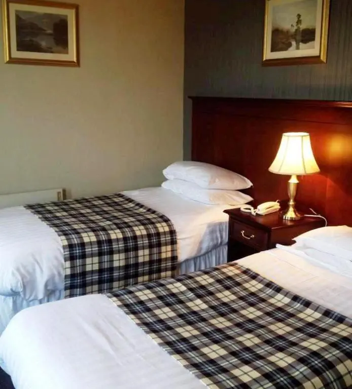a hotel room with two beds and a lamp on a table at Nethybridge Hotel in Nethy Bridge