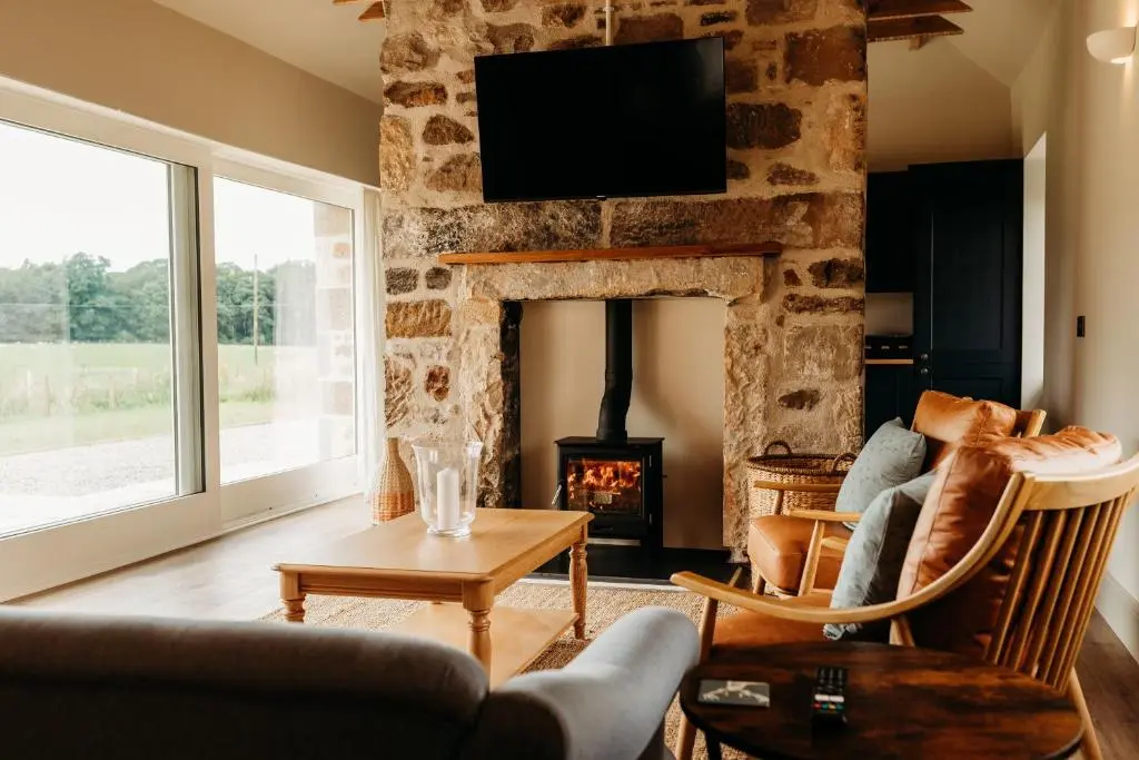 a living room with a fireplace and a tv on a stone wall at No1 Burgie Mains Cottage in Forres