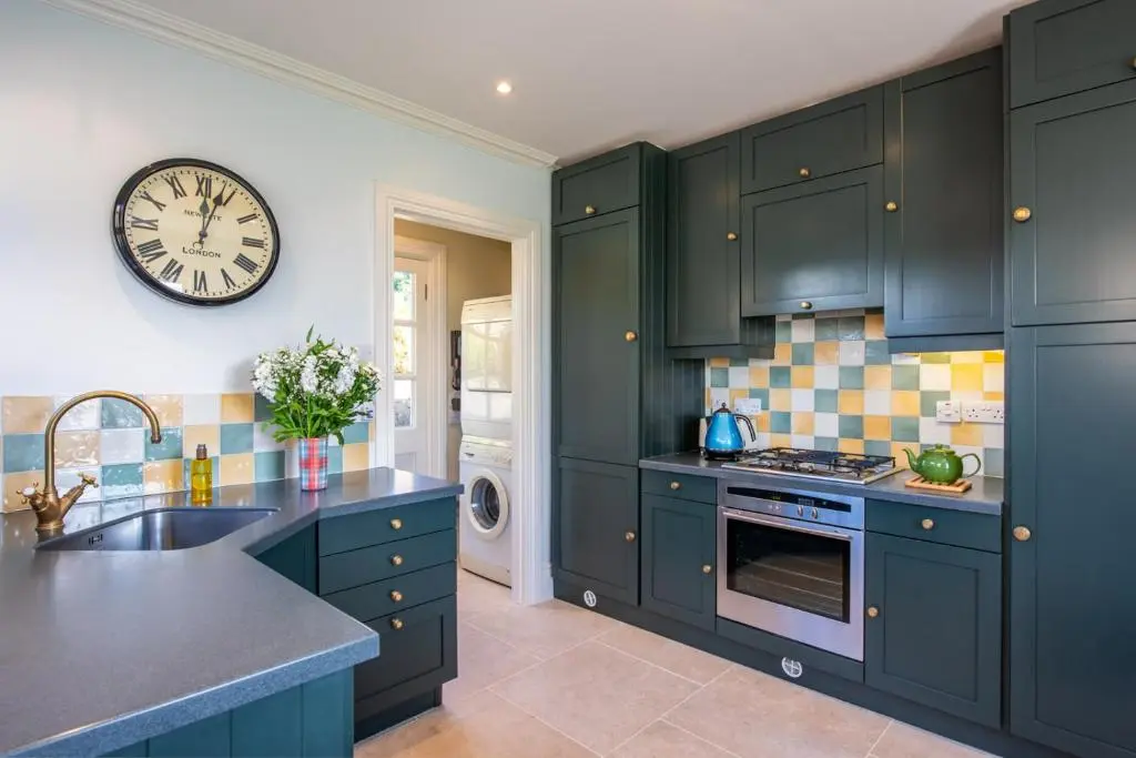 a kitchen with green cabinets and a clock on the wall at Dun Brae Cottage in Dornoch
