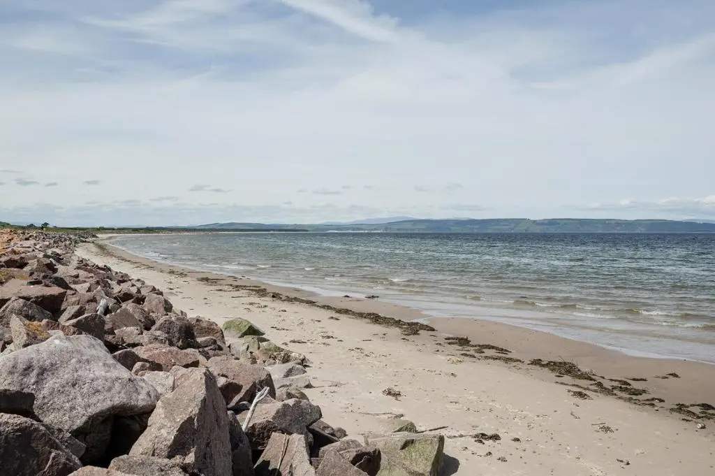 a beach with large rocks and the ocean at Fairways - Seasgair Lodges in Nairn
