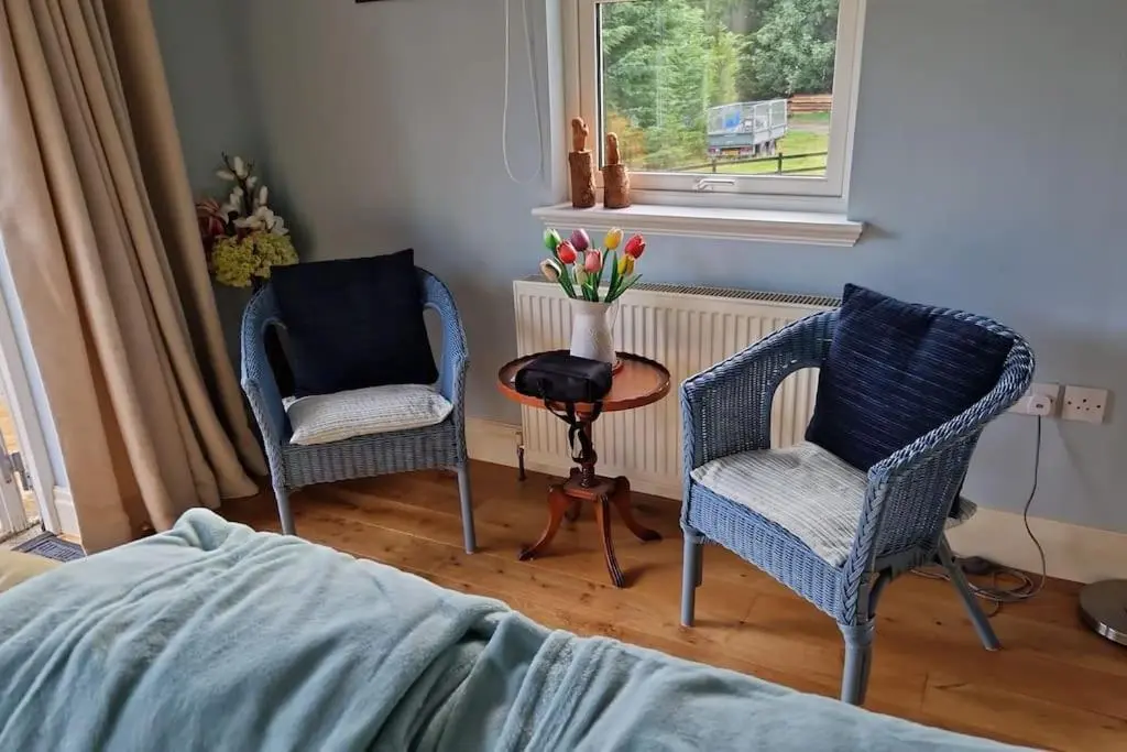 a bedroom with two chairs and a table with flowers at Heath House Loch Ness in Errogie