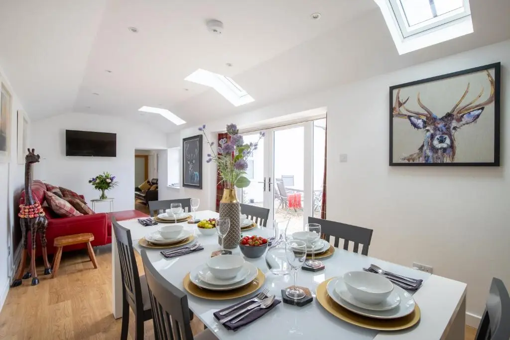 a dining room with a table with chairs and a room with a deer painting at Cairnie Cottage in Ballater