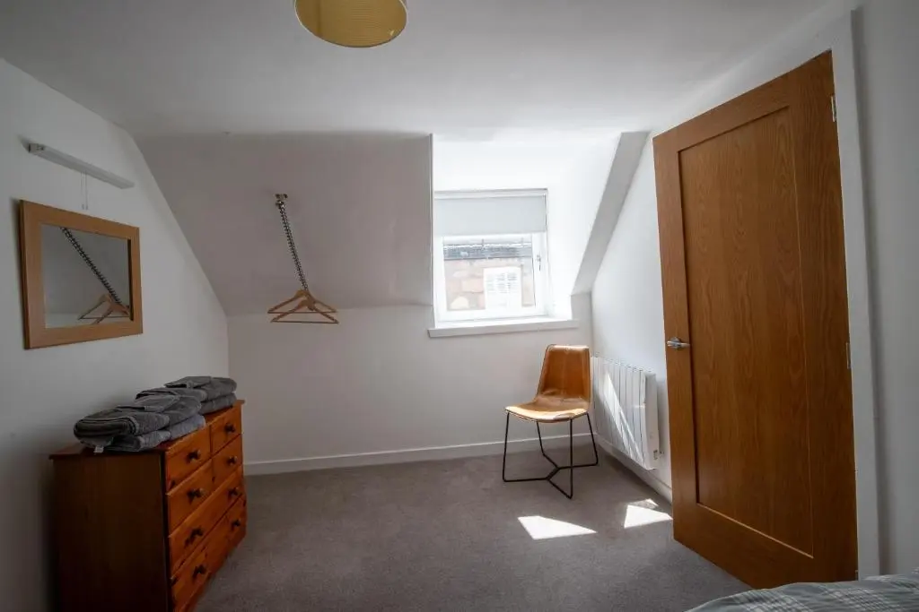 a bedroom with a bed and a dresser and a window at Cairnie Cottage in Ballater