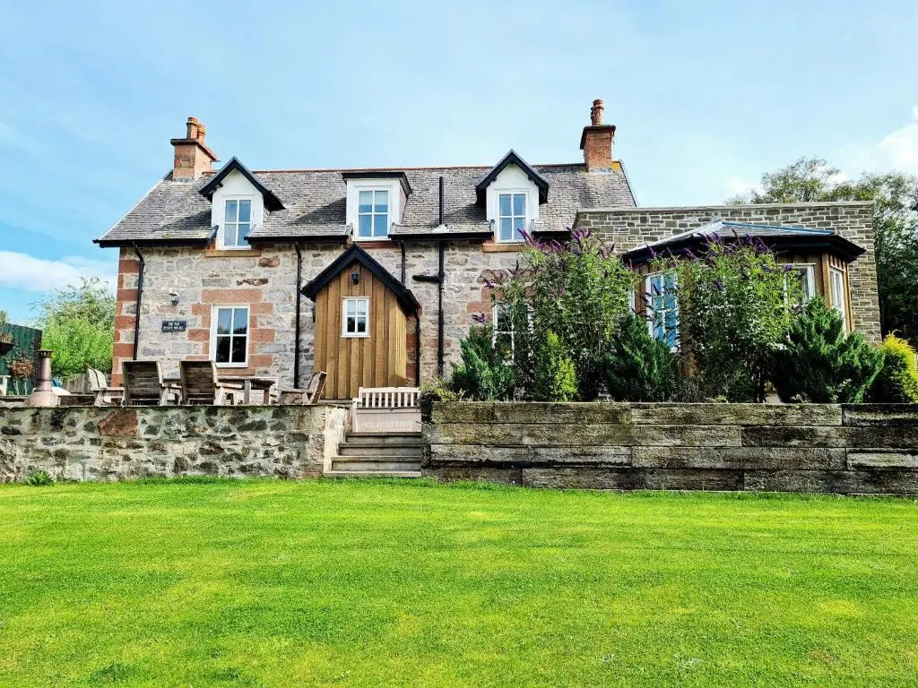 an old stone house with a stone wall and a yard at Cosy Spacious Highland Cottage in Craggie