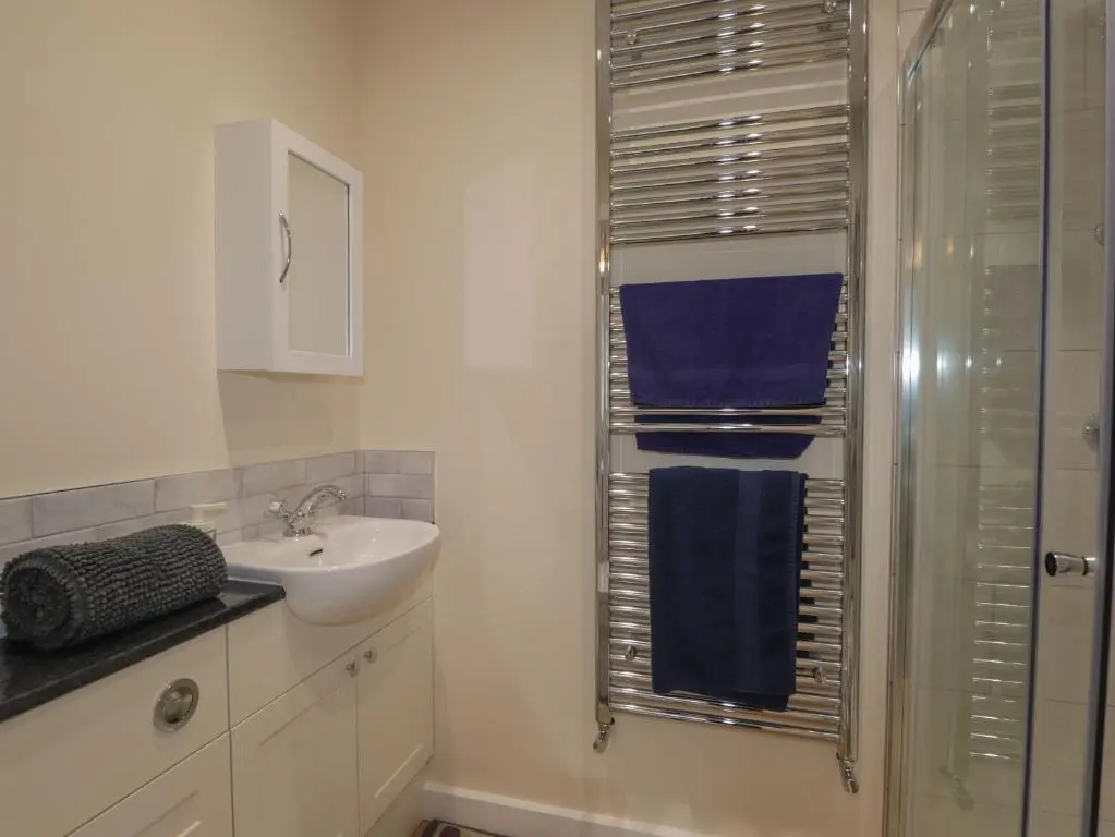 a bathroom with a sink and a shower with blue towels at Gunroom Cottage in Strathpeffer
