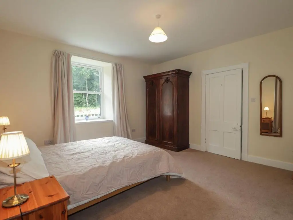 a bedroom with a bed and a dresser and a window at Gunroom Cottage in Strathpeffer