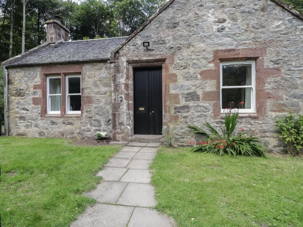 an old stone house with a black door at Gunroom Cottage in Strathpeffer