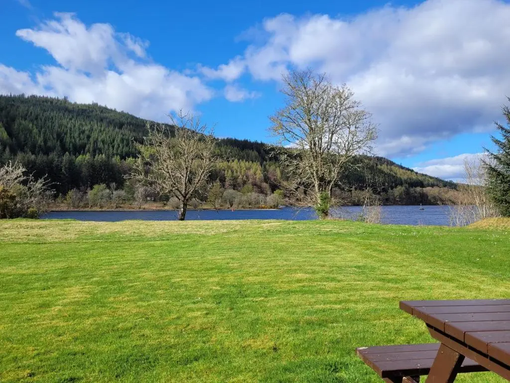a picnic table in a field next to a lake at Lodge 2 - Inglewood Lodge in Spean Bridge