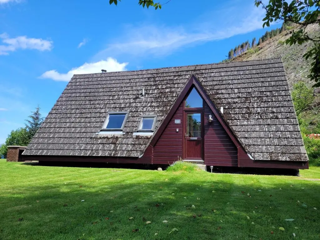 a red house with a roof on a green field at Lodge 2 - Inglewood Lodge in Spean Bridge
