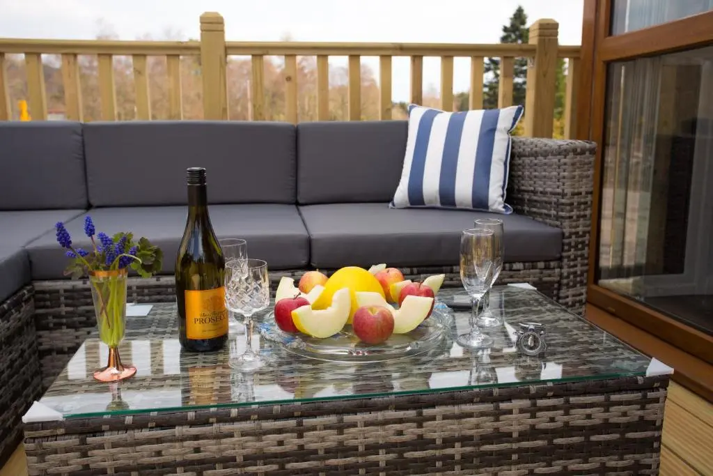 a glass table with a bowl of fruit and a bottle of wine at Bluebell Lodge - Sleeps 4 Loch & Woodland in Strathpeffer