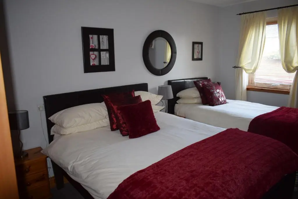 a bedroom with two beds with red pillows and a mirror at Dunroamin Self-Catering Apartment in Aviemore