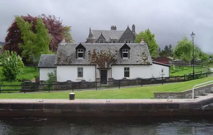 a large white house sitting next to a body of water at Old Lock-keeper's Cottage in Fort Augustus