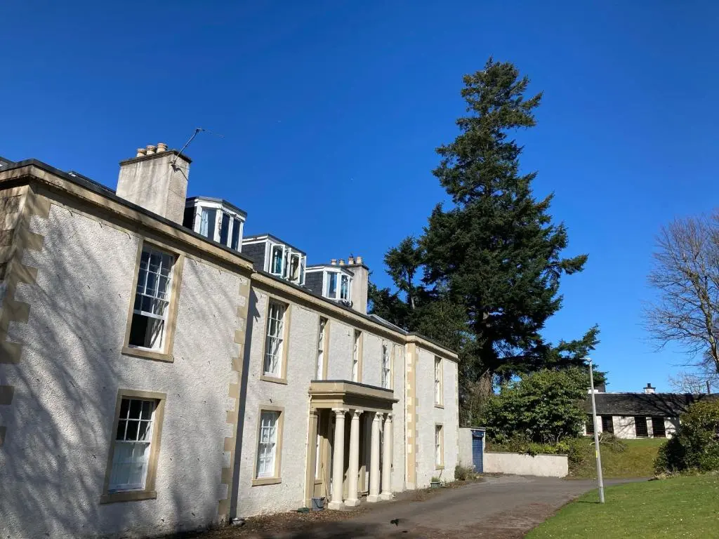 an old white building with a tree in the background at Aultnaskiach House Apartment, Inverness in Inverness
