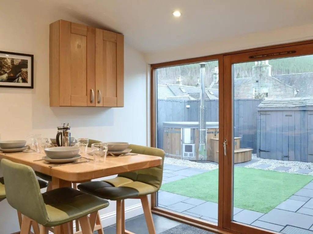 a dining room with a wooden table and a sliding glass door at Logiemar Cottage in Ballater