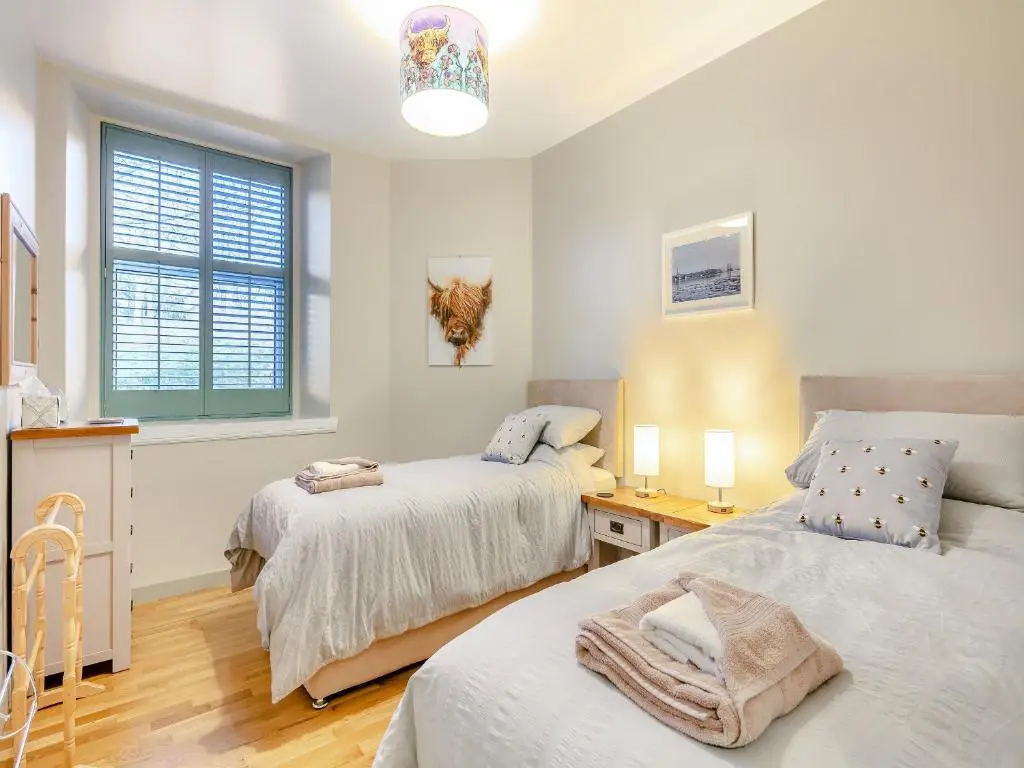a bedroom with two beds and a desk and a window at Rowan Cottage in Huntly