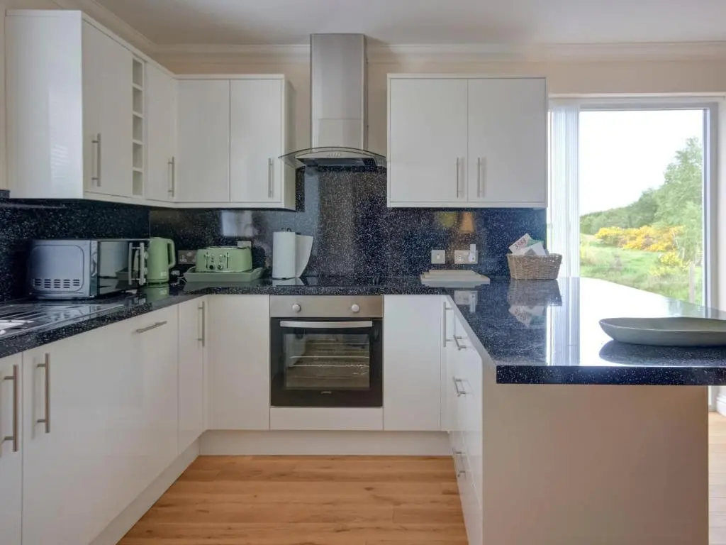 a kitchen with white cabinets and black counter tops at Darna House in Tain