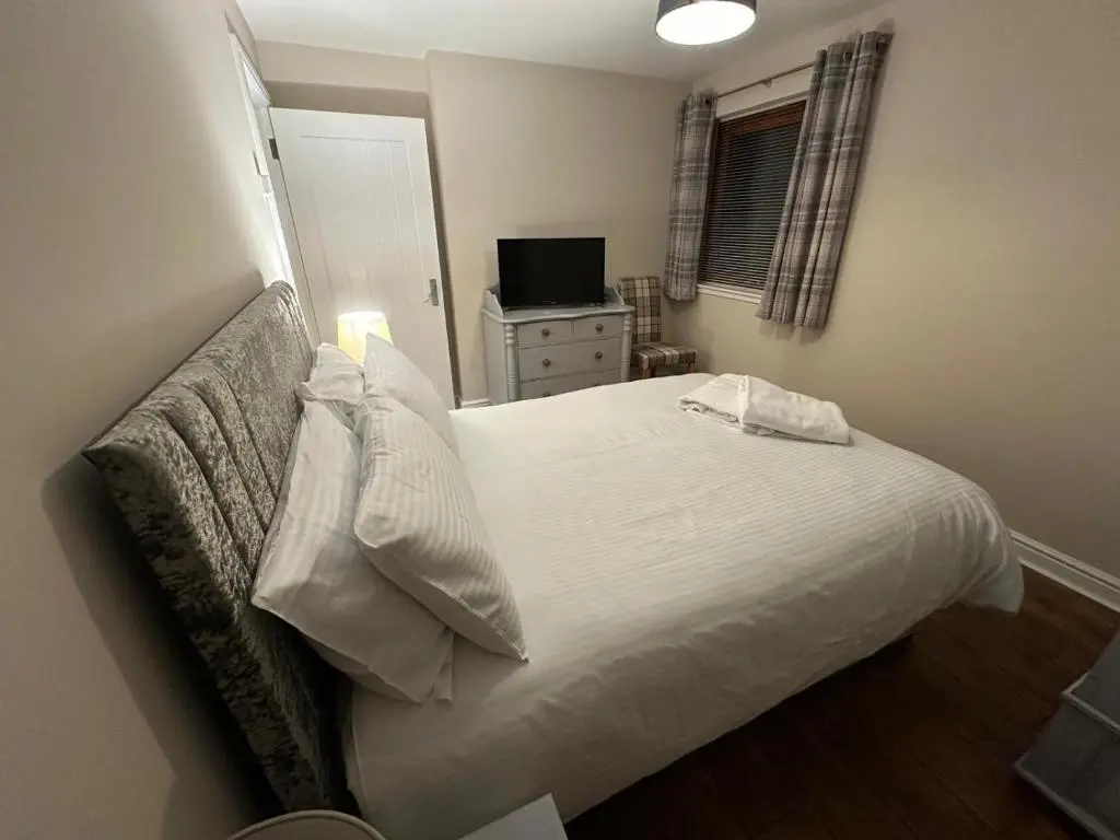 a bedroom with a white bed and a television at Pebble Cottage in Golspie