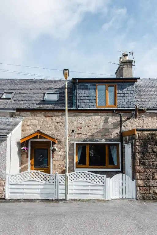 a stone house with a white fence at Mabels Cottage by the beach in Nairn