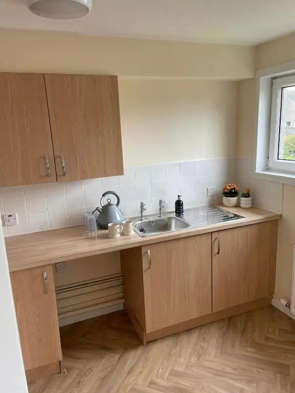 a kitchen with wooden cabinets and a sink and a window at Wick Bay Apartments in Wick
