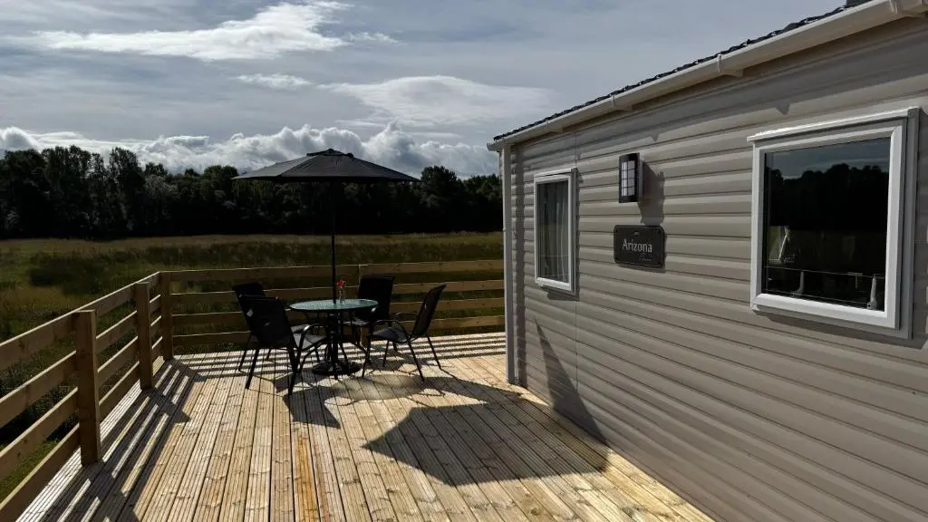a deck with a table and chairs and an umbrella at Wildcat Lodge Grantown on Spey in Grantown on Spey