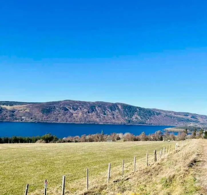 a fence in a field next to a body of water at The Pod at Loch Ness Heights at Athbhinn, IV26TU in Inverness