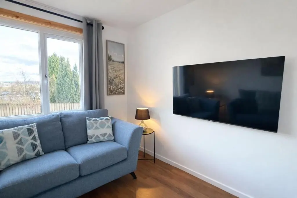 a living room with a blue couch and a large flat screen tv at Charlie's View in Inverness