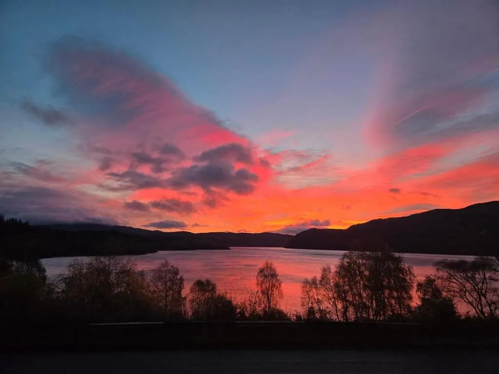 a sunset over a body of water with mountains at Luichart Lodge in Lochluichart Station