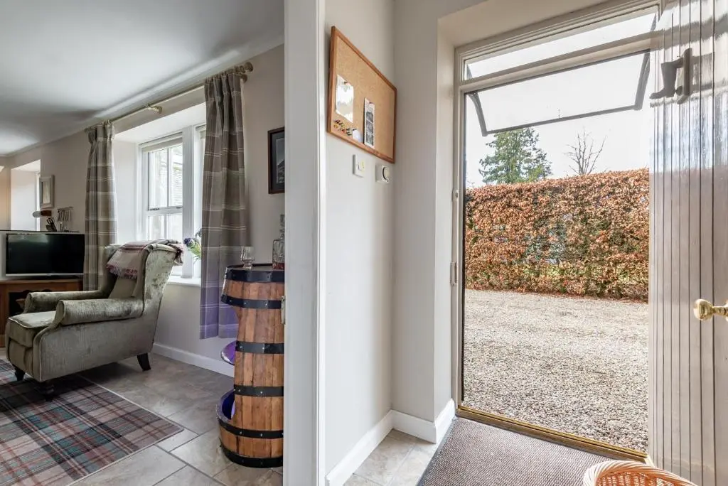 a living room with a sliding glass door and a chair at Falls Cottage in Glenlivet