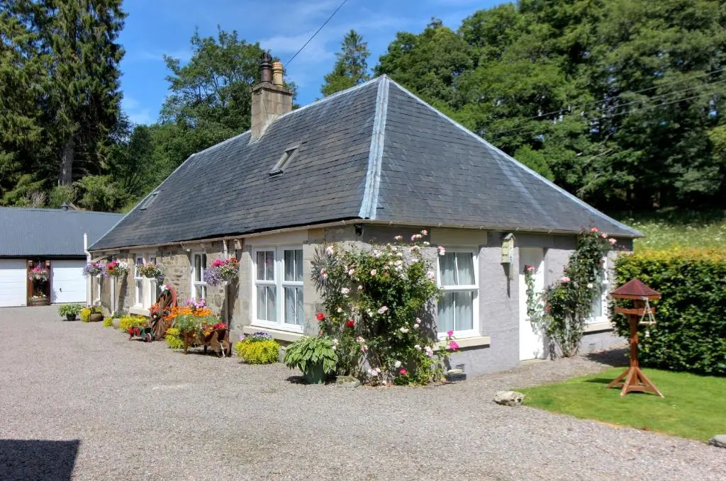 a white house with flowers in front of it at Falls Cottage in Glenlivet