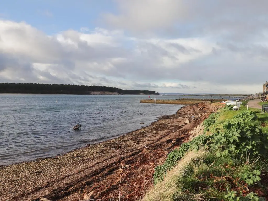 a body of water with a beach and a pier at Bayside Cottage in Forres