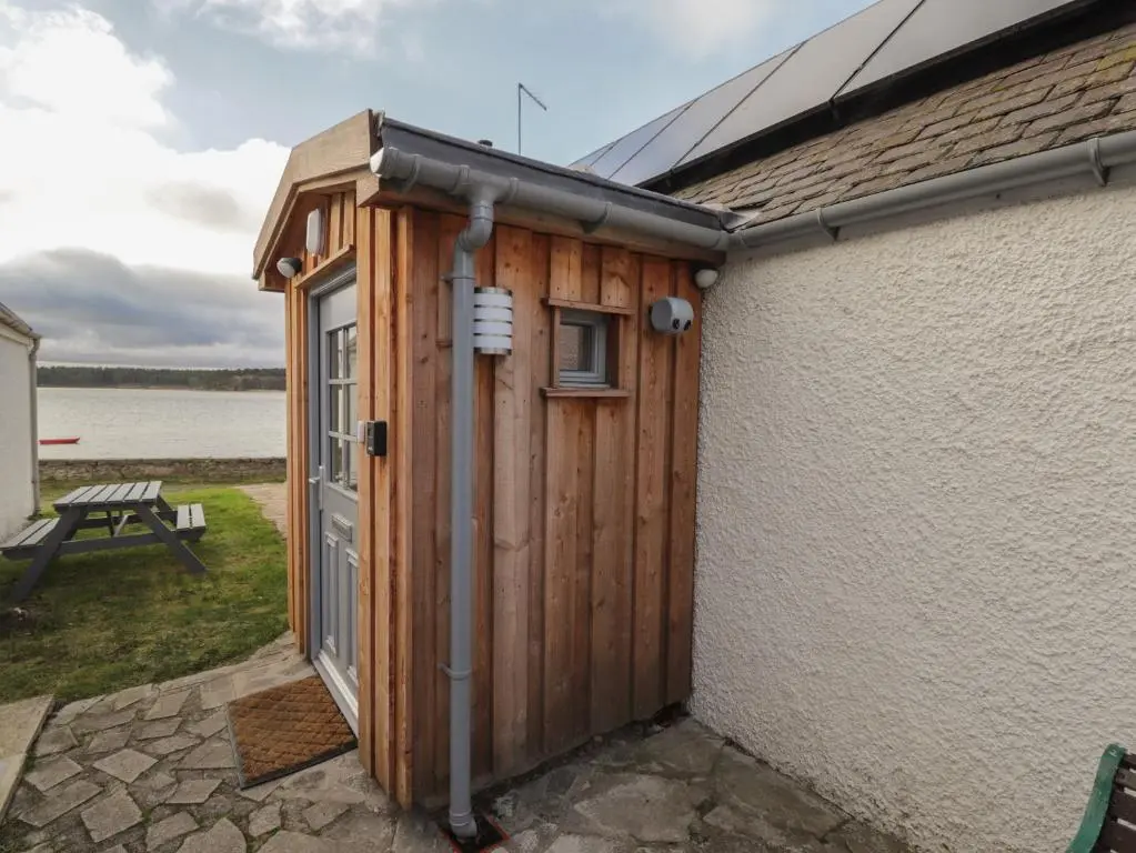 a wooden shed with a door on the side of a building at Bayside Cottage in Forres